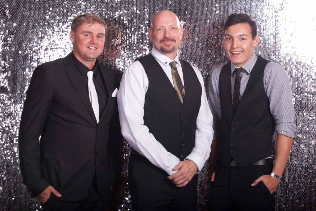 Three men in formal clothes standing in front of sequin background