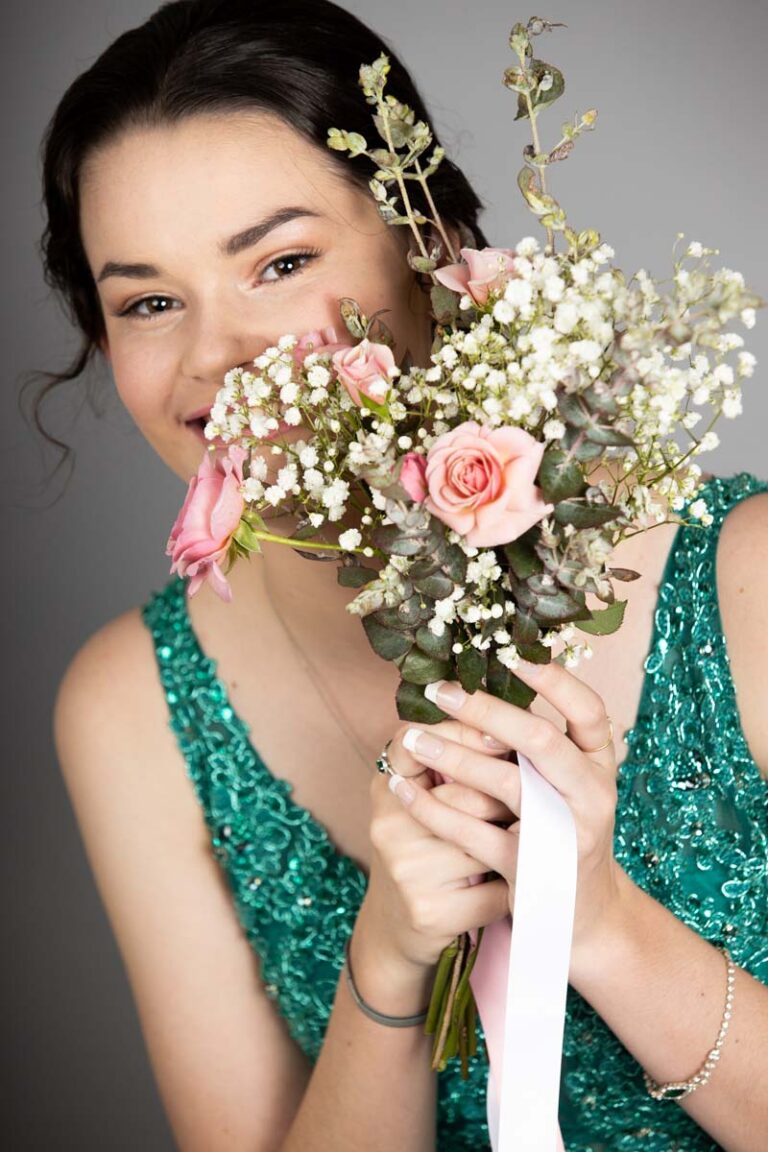 Young woman in formal dress hiding behind bouquet of flowers