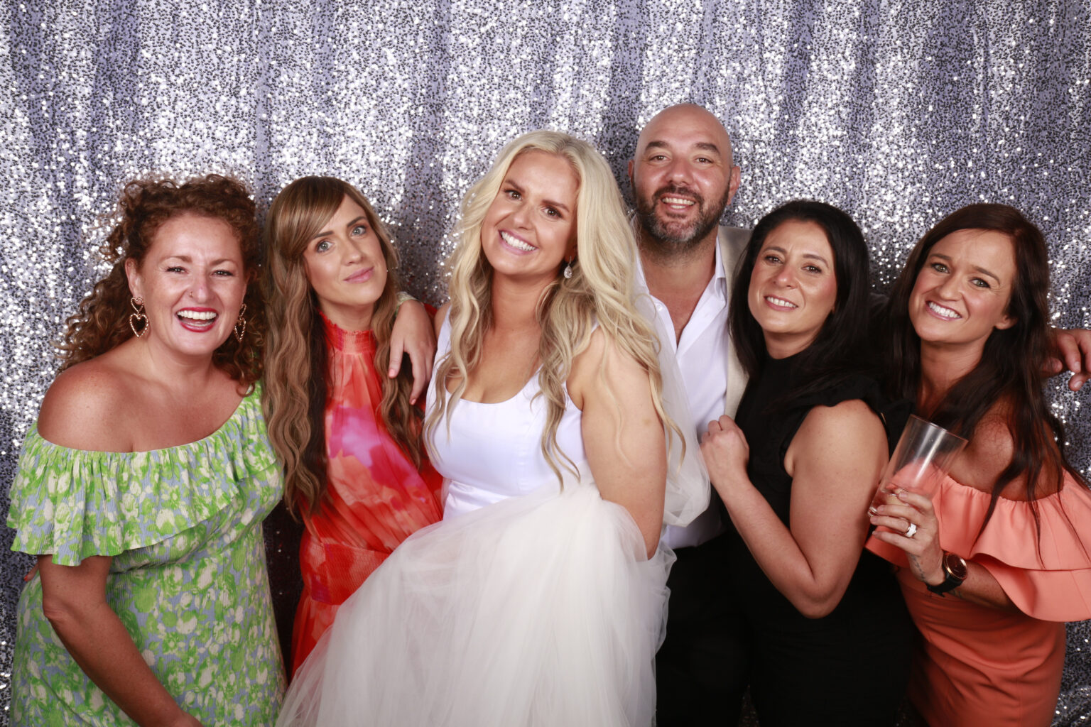 bride and husband with friends in photo booth with a silver sequin background