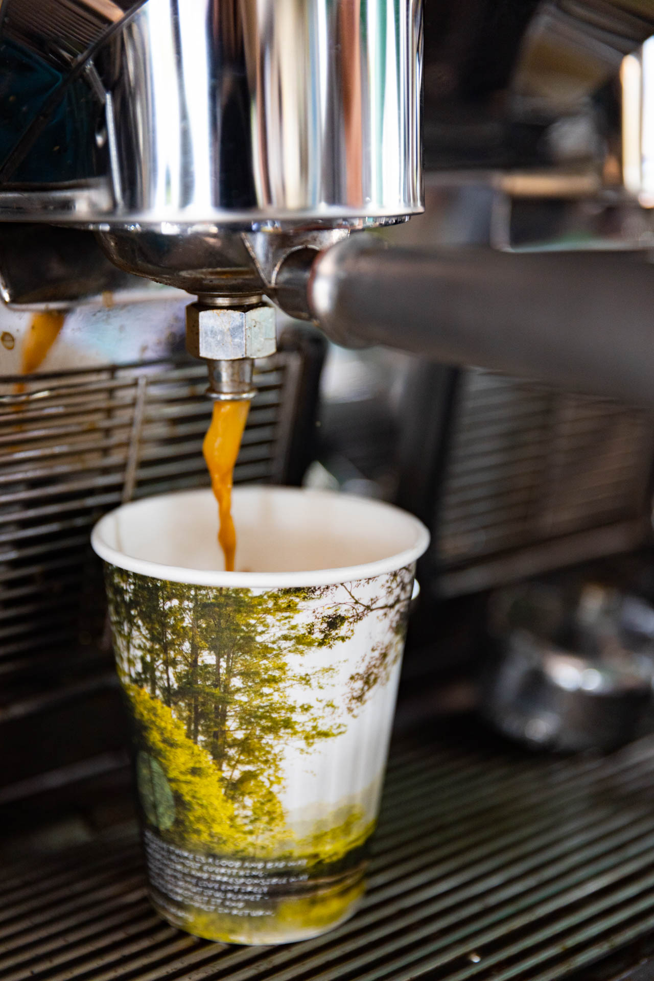 product photo of a paper cup in coffee machine with coffee pouring